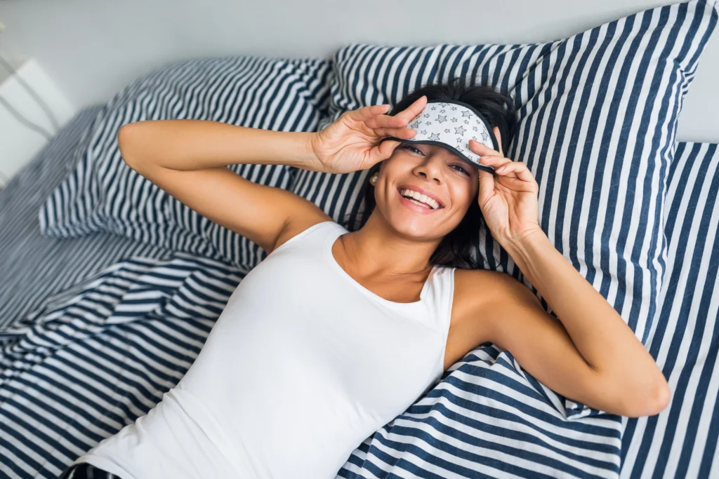 Mulher relaxada na cama, sorrindo ao acordar, destacando a influência do sono na recuperação e na saúde metabólica.