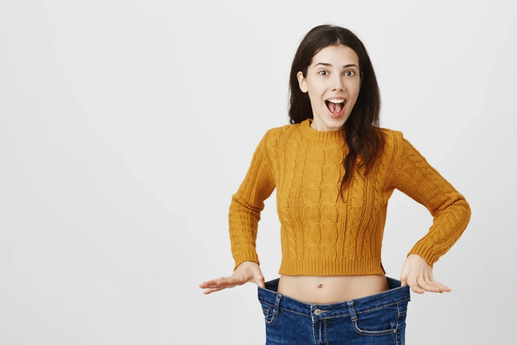 Mulher feliz segurando a calça folgada, demonstrando os resultados de uma dieta e estilo de vida saudáveis.