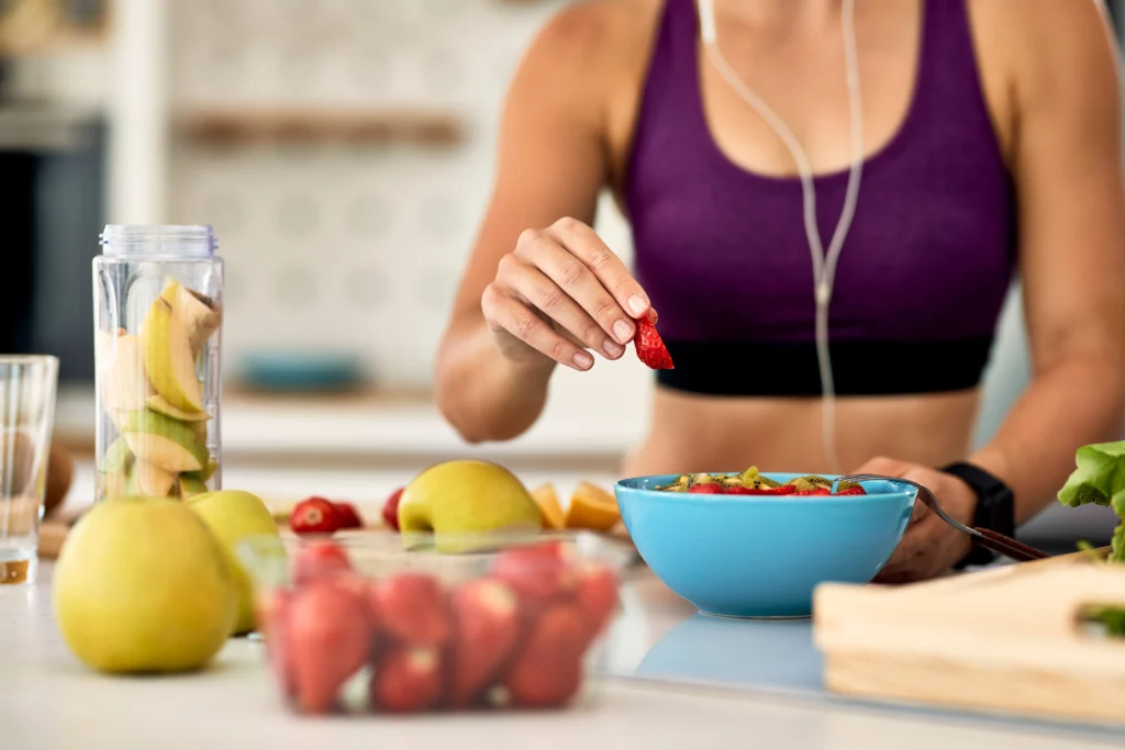 Mulher adicionando morangos a uma salada de frutas, representando a alimentação equilibrada para a saúde metabólica.