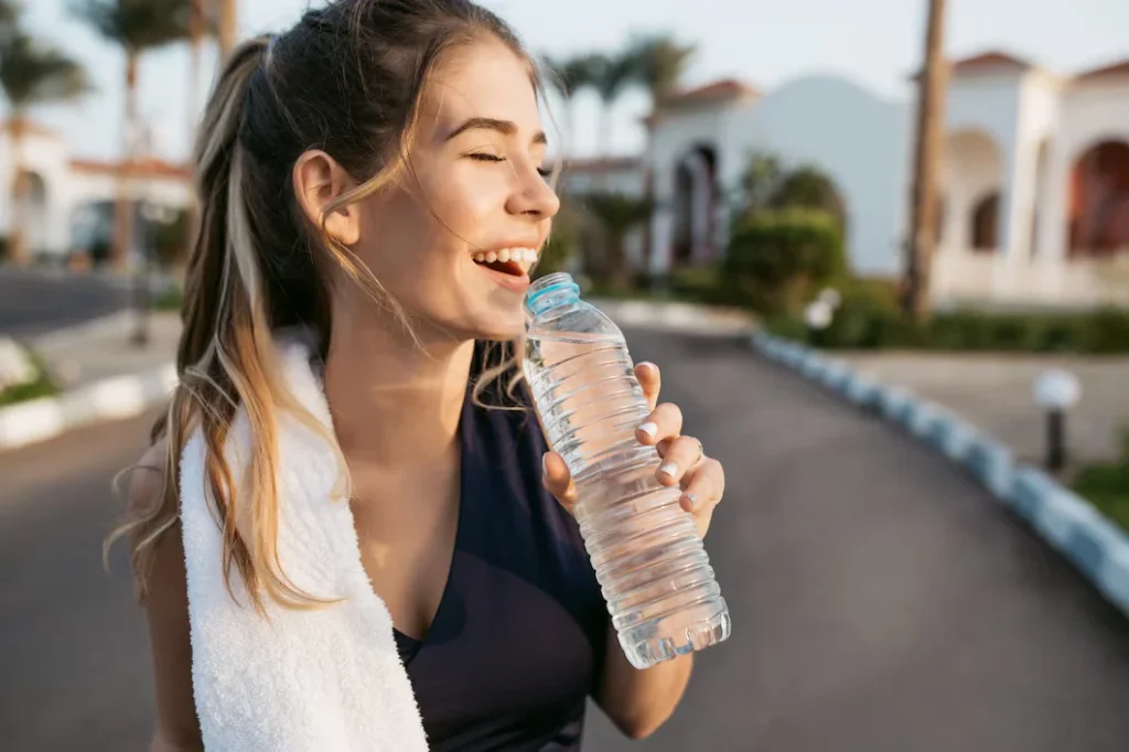 Calculadora de Hidratação: Mulher feliz segurando uma garrafa de água sob o sol, destacando a importância da hidratação adequada.