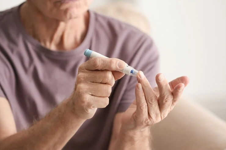Idoso com diabetes verificando a glicemia em casa, reforçando a importância do controle de condições metabólicas.