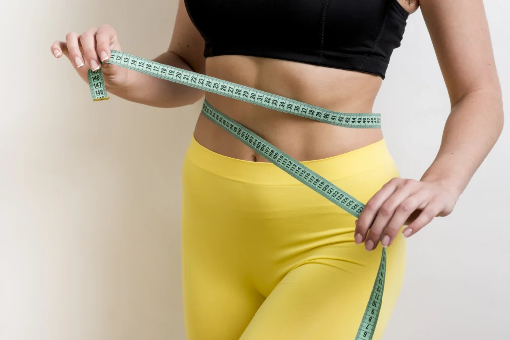 Mulher fitness medindo a cintura com fita métrica, representando o impacto da calculadora de Taxa de Metabolismo Basal no controle de peso.