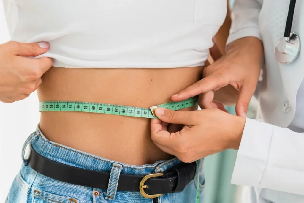 Profissional de saúde medindo a circunferência abdominal de uma mulher, avaliando riscos metabólicos e cardiovasculares.