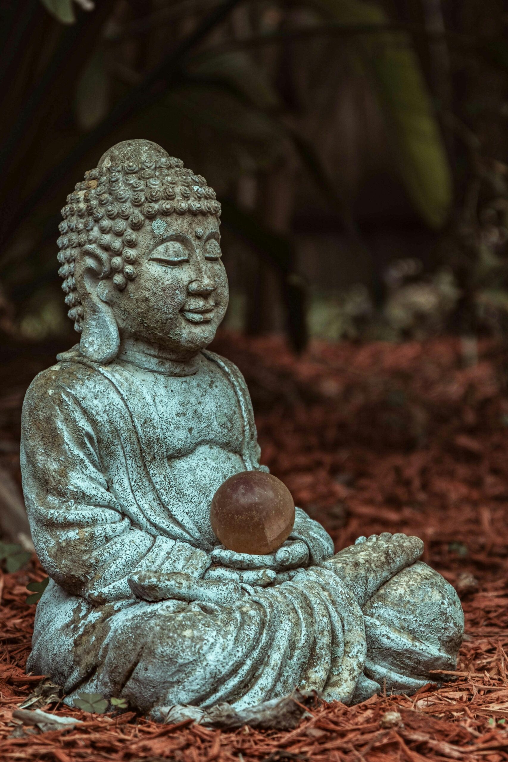 Como cuidar da saúde mental: Estátua de Buda com esfera nas mãos, rodeada por natureza, representando mindfulness e equilíbrio mental.