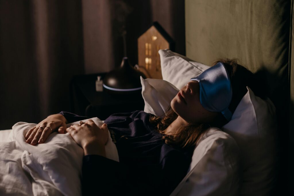 Mulher deitada na cama com máscara de dormir azul, simbolizando a importância do sono para a recuperação e bem-estar.
