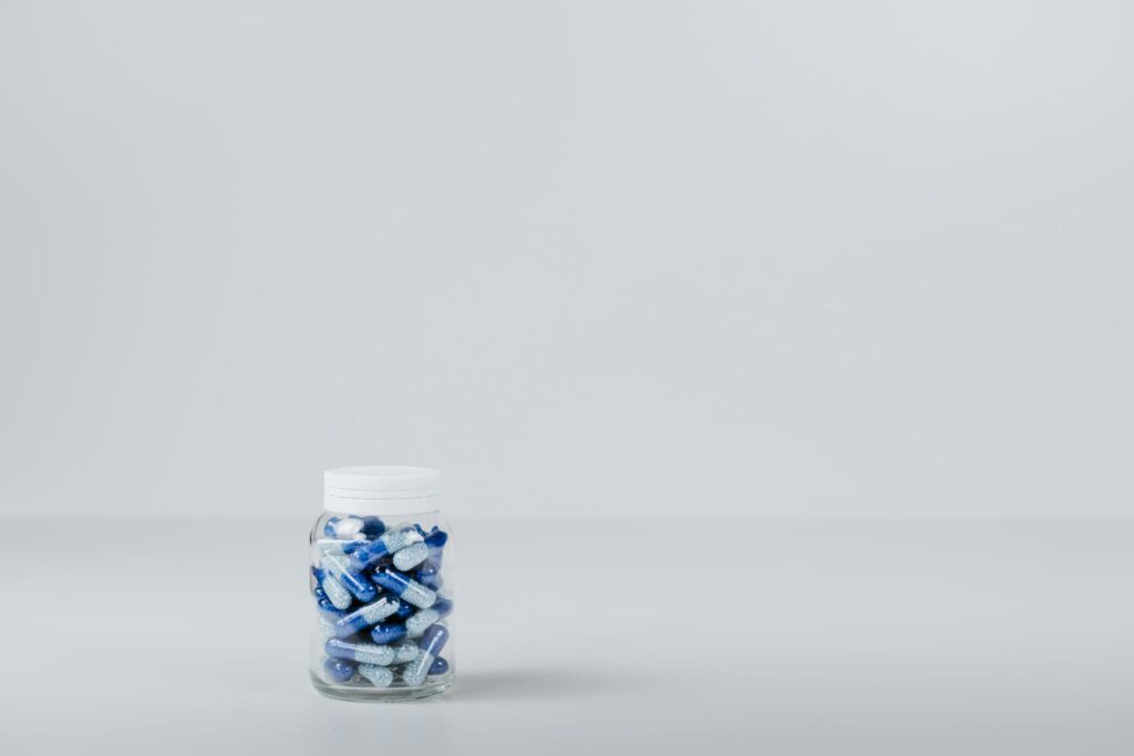 Frasco com cápsulas azuis e brancas sobre a mesa, ilustrando o que é testosterona e sua associação com suplementos hormonais.