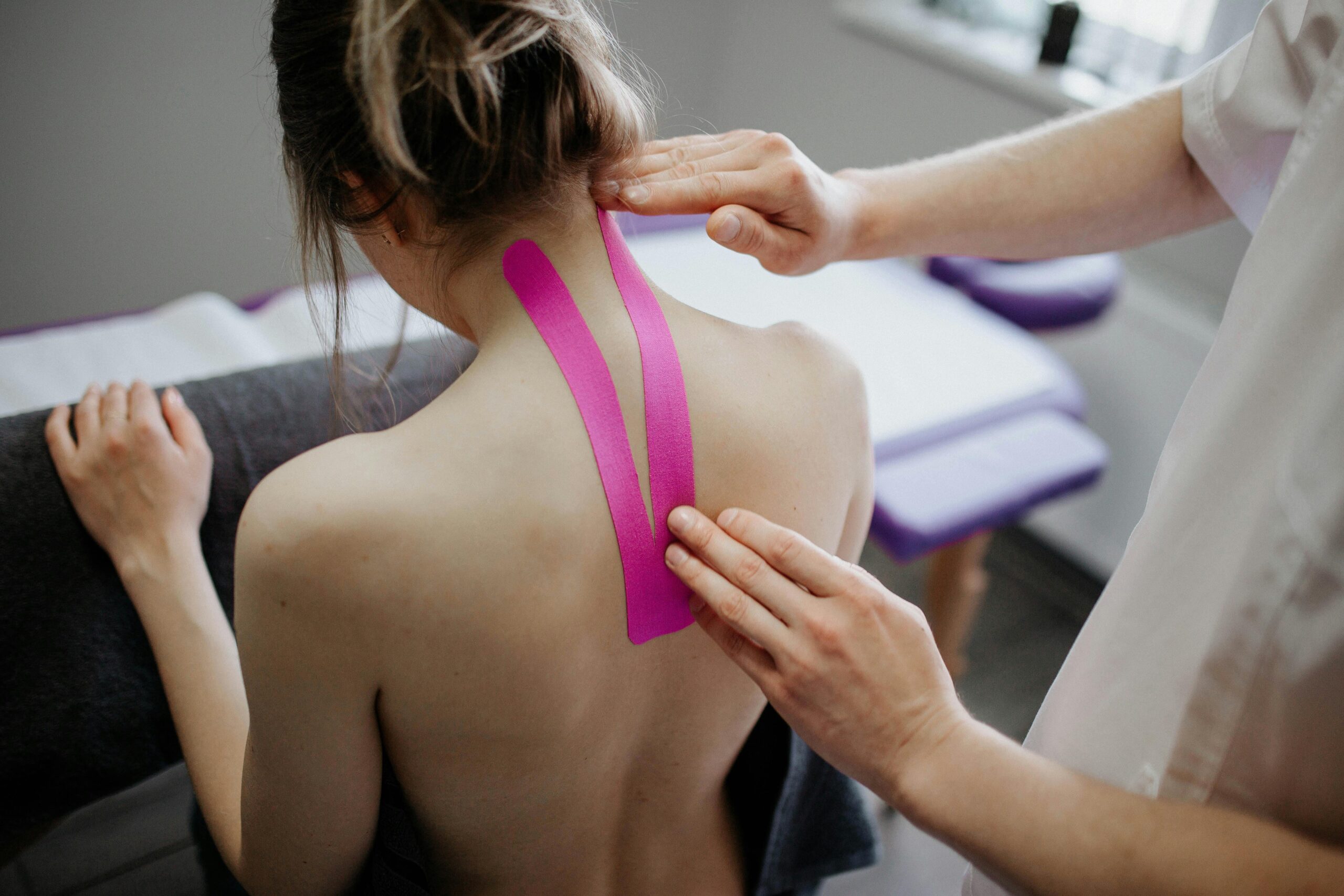 Como recuperar a energia do corpo rapidamente? na imagem uma moça jovem aplicando fitas de kinesio na região de trapézio e rombóides por profissional da saúde.