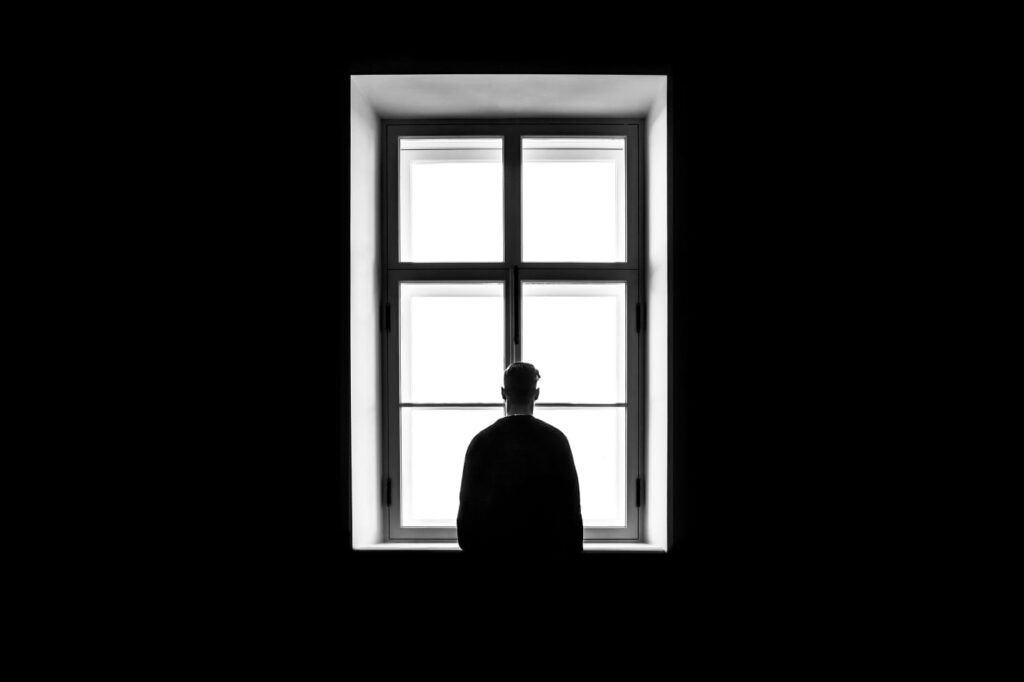 Pessoa olhando pela janela, simbolizando reflexão e a importância da observação pessoal para identificar sinais de transtornos mentais.