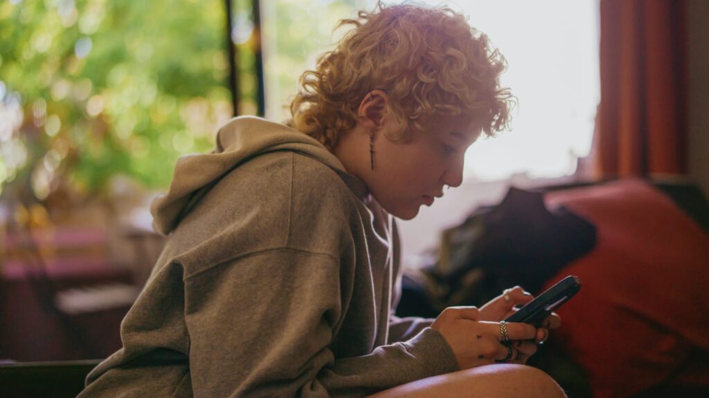Adolescente com fones de ouvido olhando pensativo, sentado em sala.