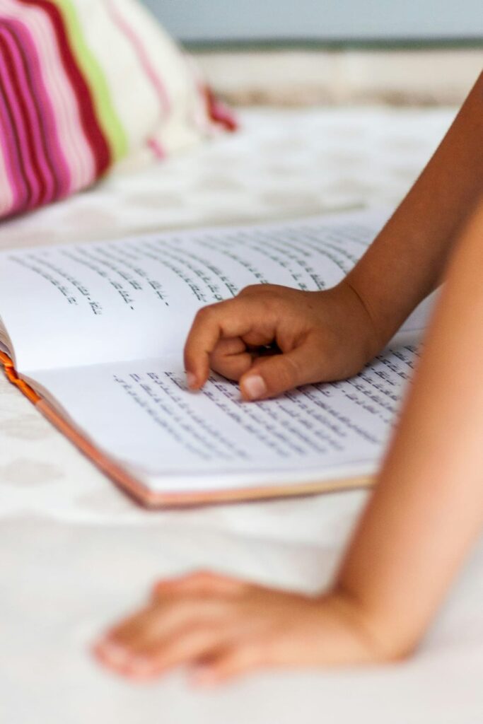 Braços de uma criança escrevendo em caderno escolar com lápis.