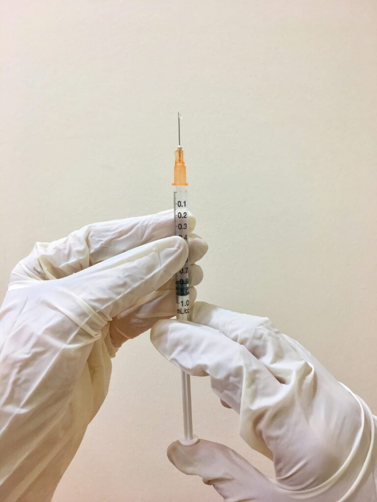 Mãos enluvadas segurando uma seringa com medicamento, prontas para aplicação.