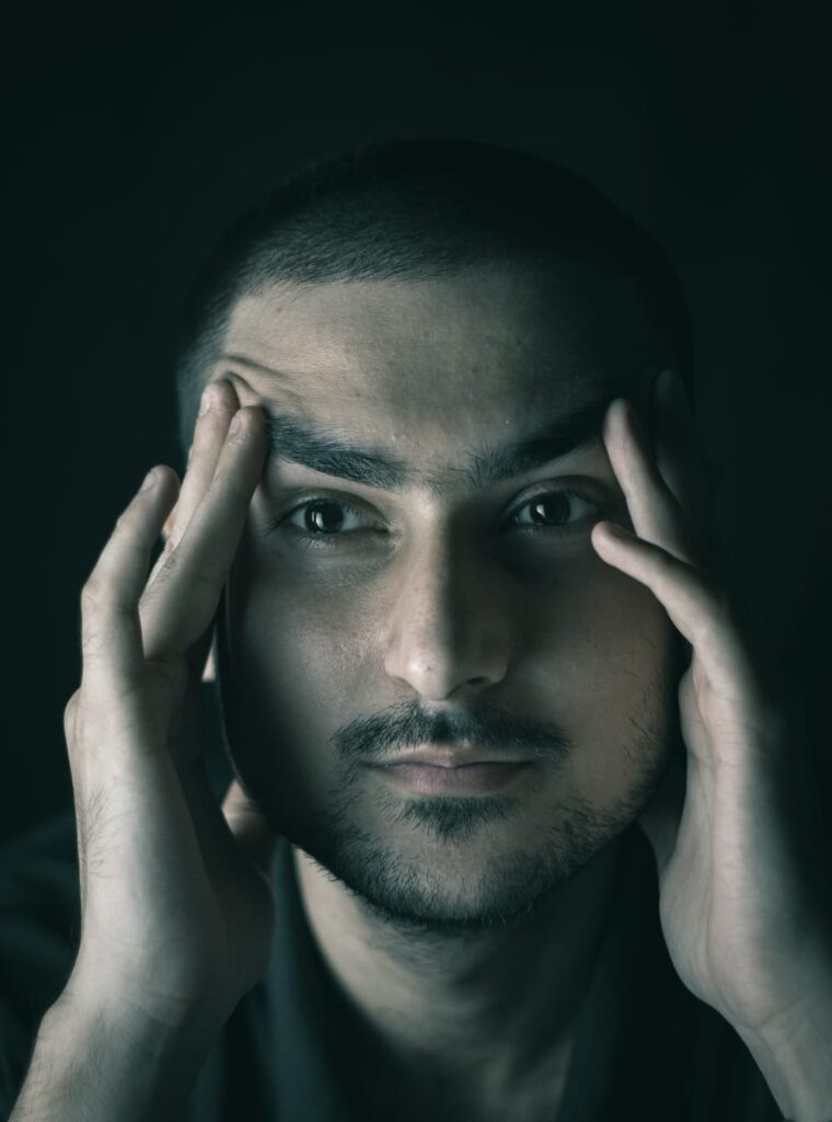 Homem com expressão de estresse cobrindo as têmporas com as mãos.