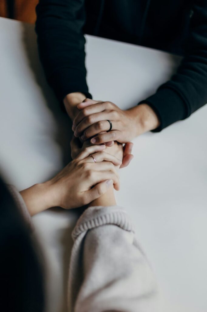 Duas pessoas segurando as mãos em gesto de apoio emocional.