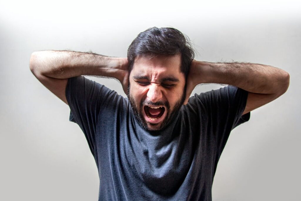 Pessoa gritando com as mãos nos ouvidos, expressando angústia e sobrecarga mental.