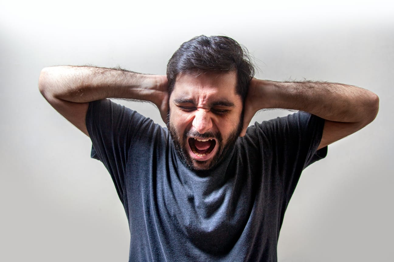 Pessoa gritando com as mãos nos ouvidos, expressando angústia e sobrecarga mental.
