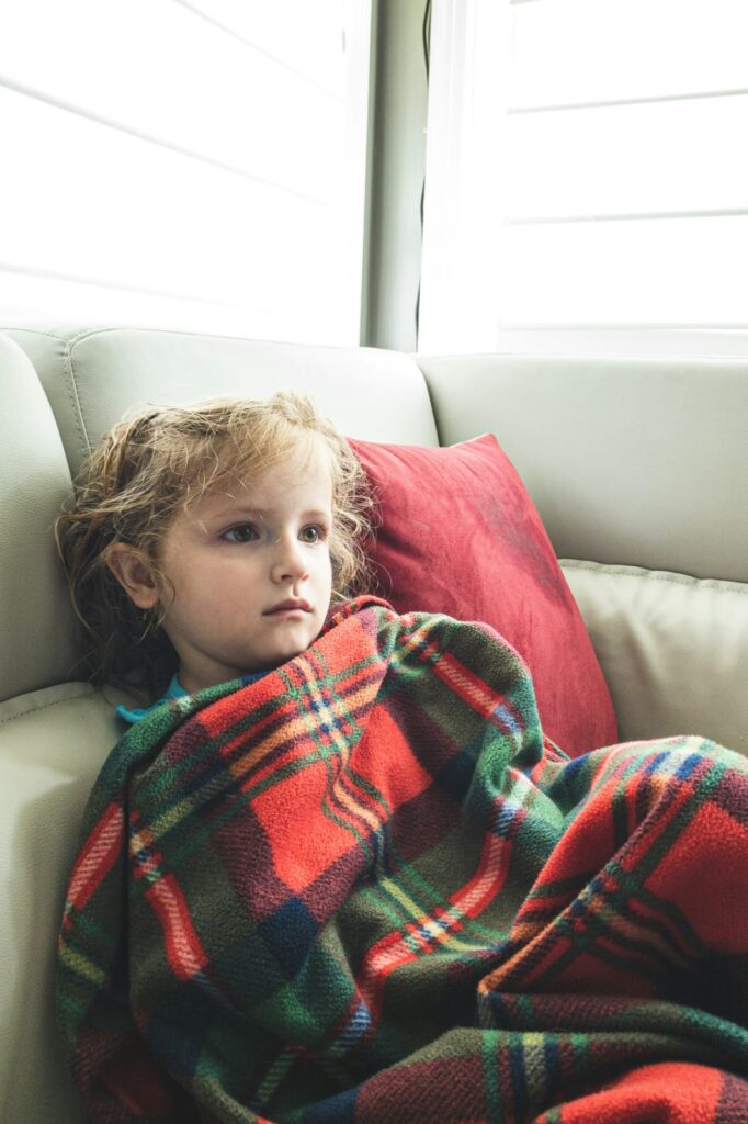 Criança doente com gripe deitada no sofá coberta com uma manta.