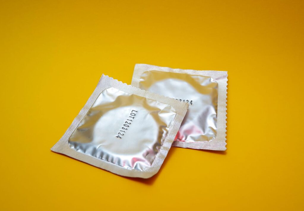 Dois preservativos masculinos sobre uma superfície amarela, sugerindo práticas seguras de saúde sexual.
