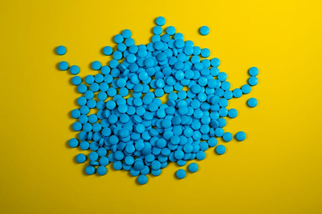 Comprimidos azuis sobre uma superfície amarela, representando medicamentos como a Tadalafila.