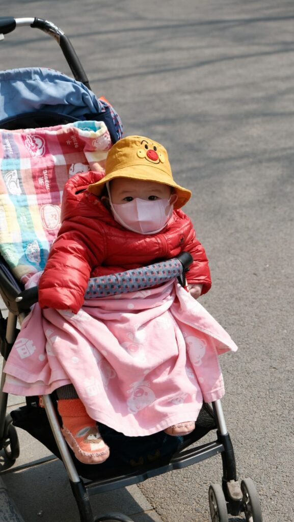Bebê de máscara no carrinho protegido contra coqueluche.