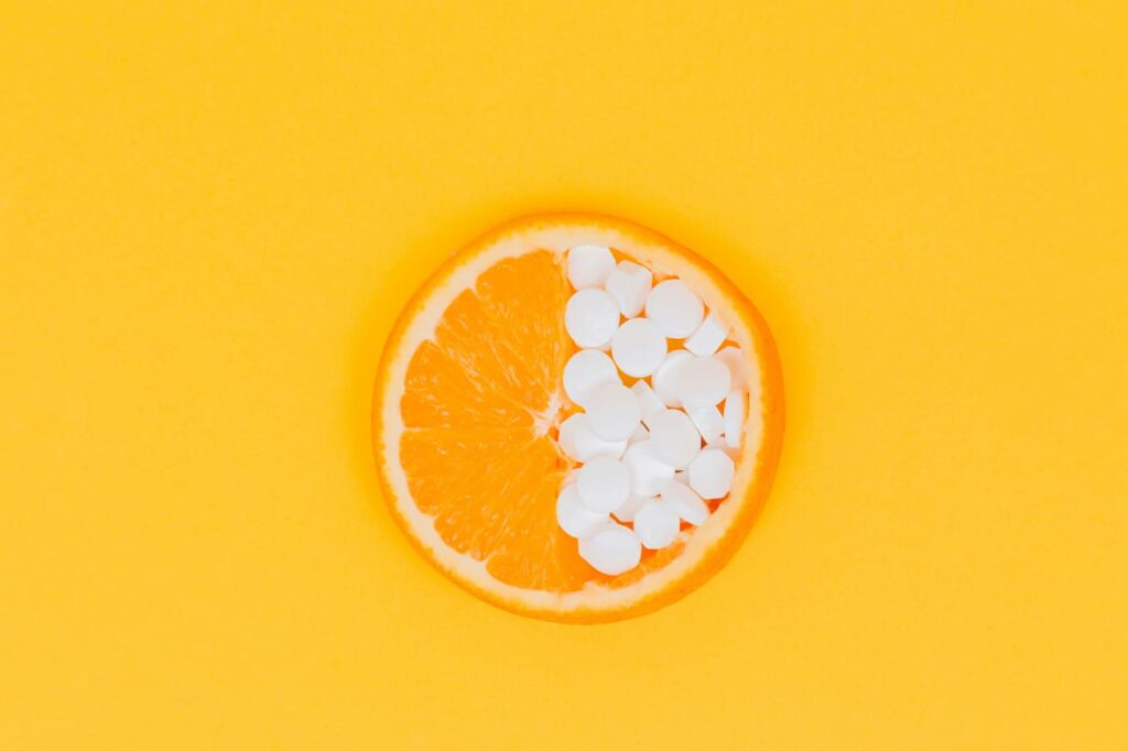 Laranja com comprimidos ilustrando o uso de vitamina C como suplemento antioxidante.