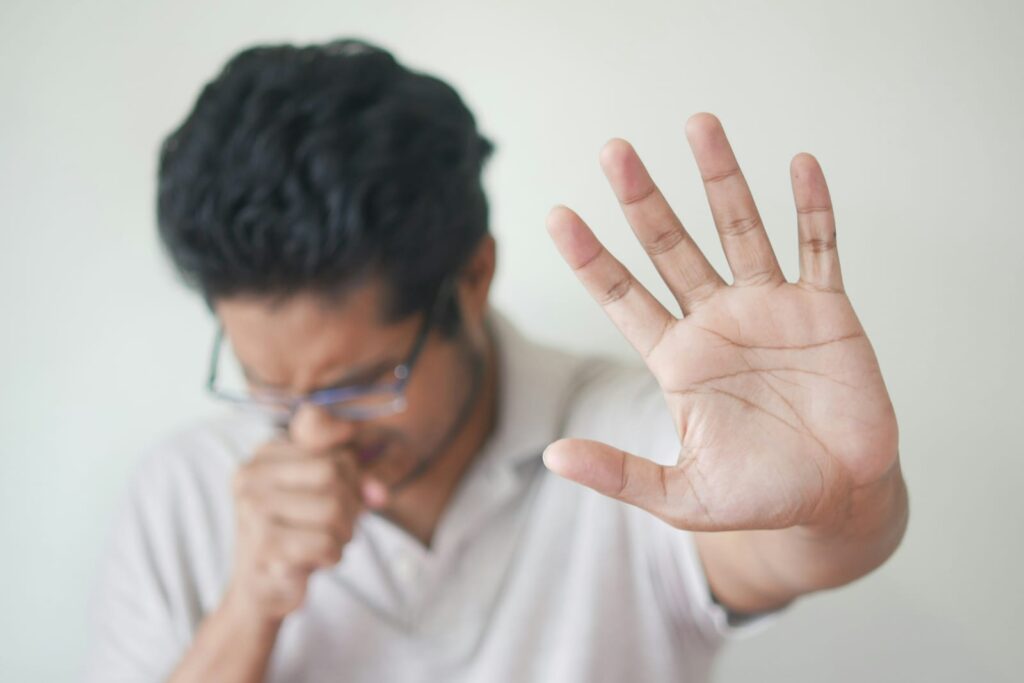 Homem gripado tossindo e levantando a mão, relacionado ao uso de vitamina C para gripe.