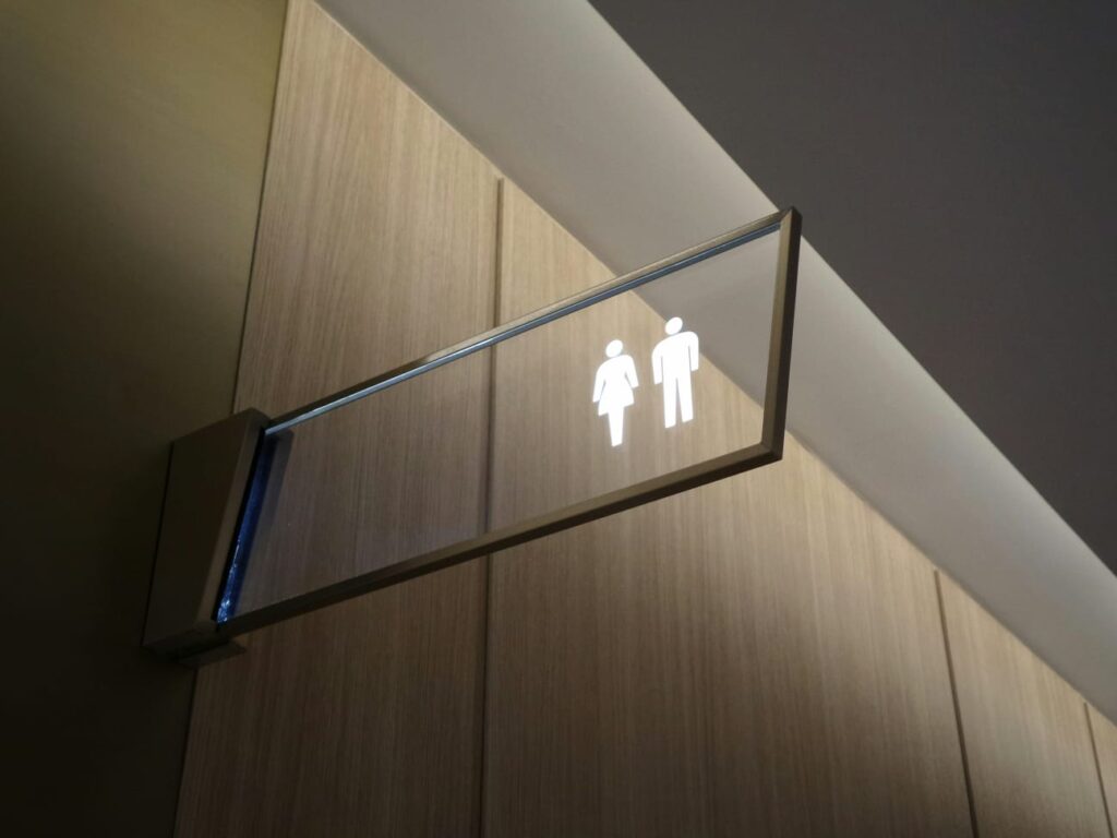 Placa iluminada de banheiro feminino e masculino, representando a relação entre urina e infecção urinária na gravidez.