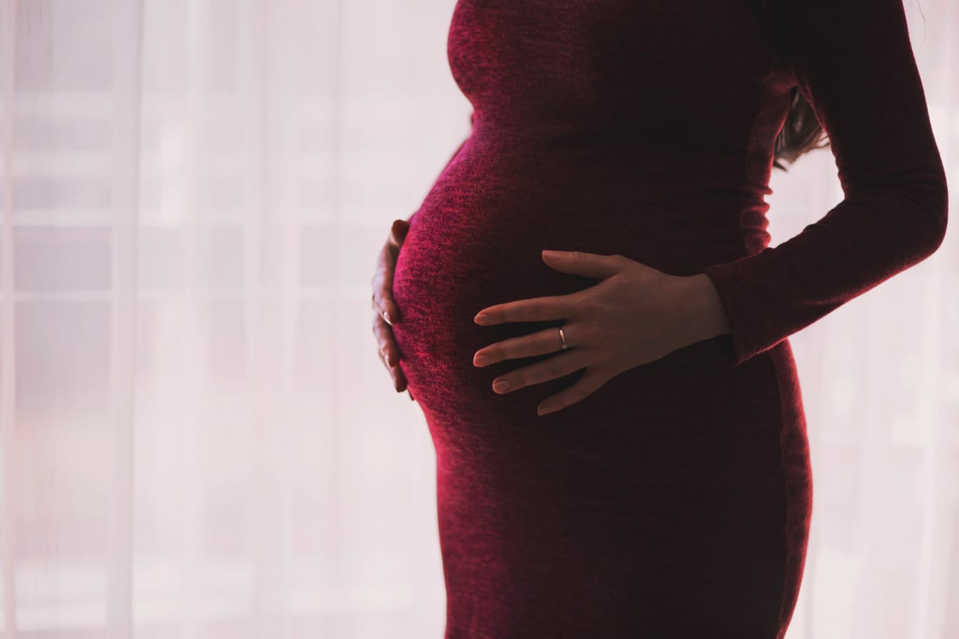 Mulher grávida com as mãos sobre a barriga, ilustrando a importância do uso de ácido fólico na gravidez.