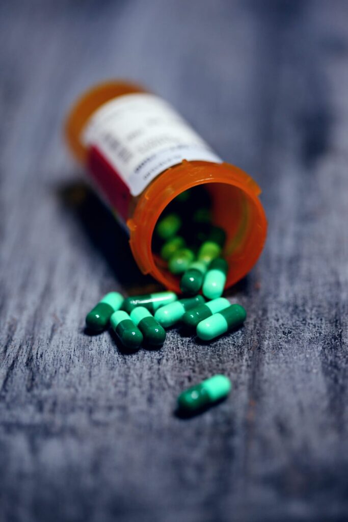 Frasco de cápsulas derramado em superfície, simbolizando a interação medicamentosa.