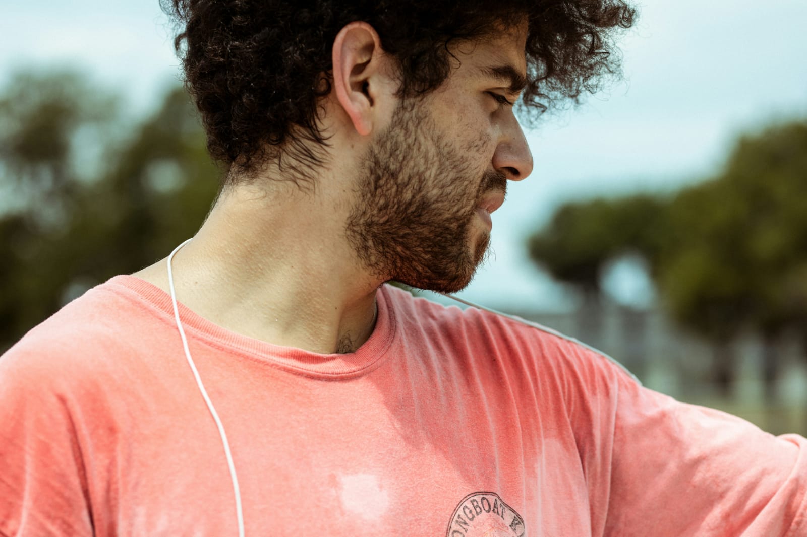 Homem jovem com camiseta rosa transpirando após esforço físico ao ar livre.