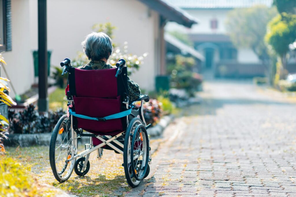 Idosa em cadeira de rodas ao ar livre, representando os desafios de mobilidade e cuidados no Alzheimer.