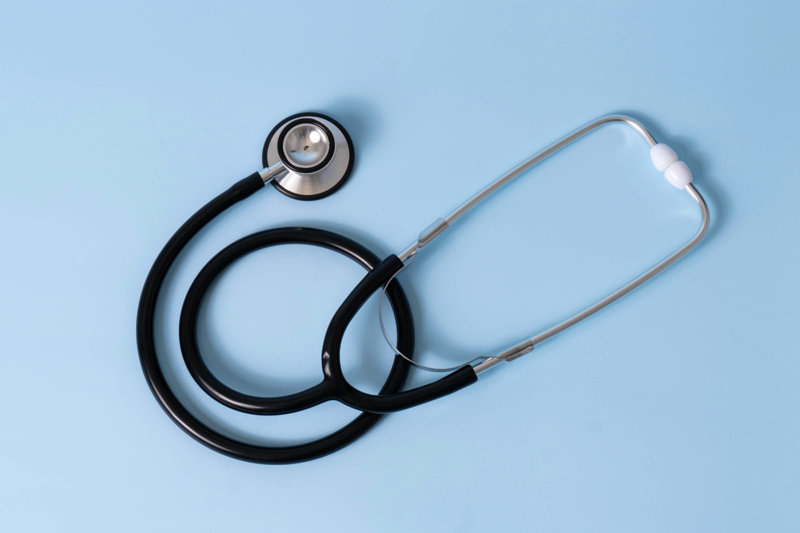 Estetoscópio preto e prateado sobre fundo azul claro, símbolo do cuidado médico e da saúde cardiovascular.