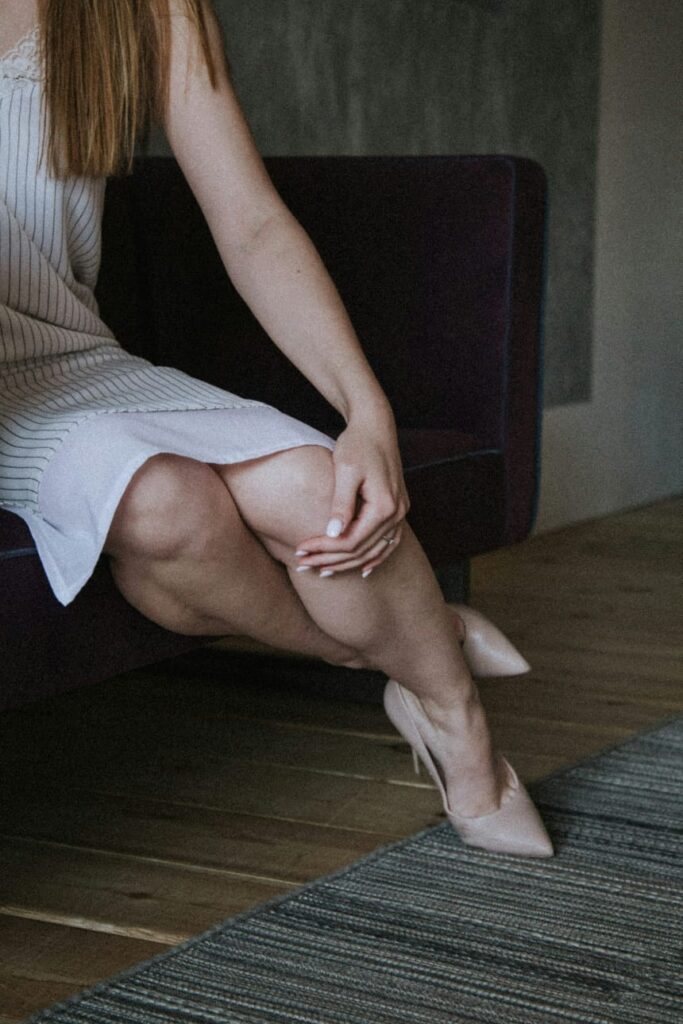 Mulher sentada com dor na perna, sintoma comum de trombose.