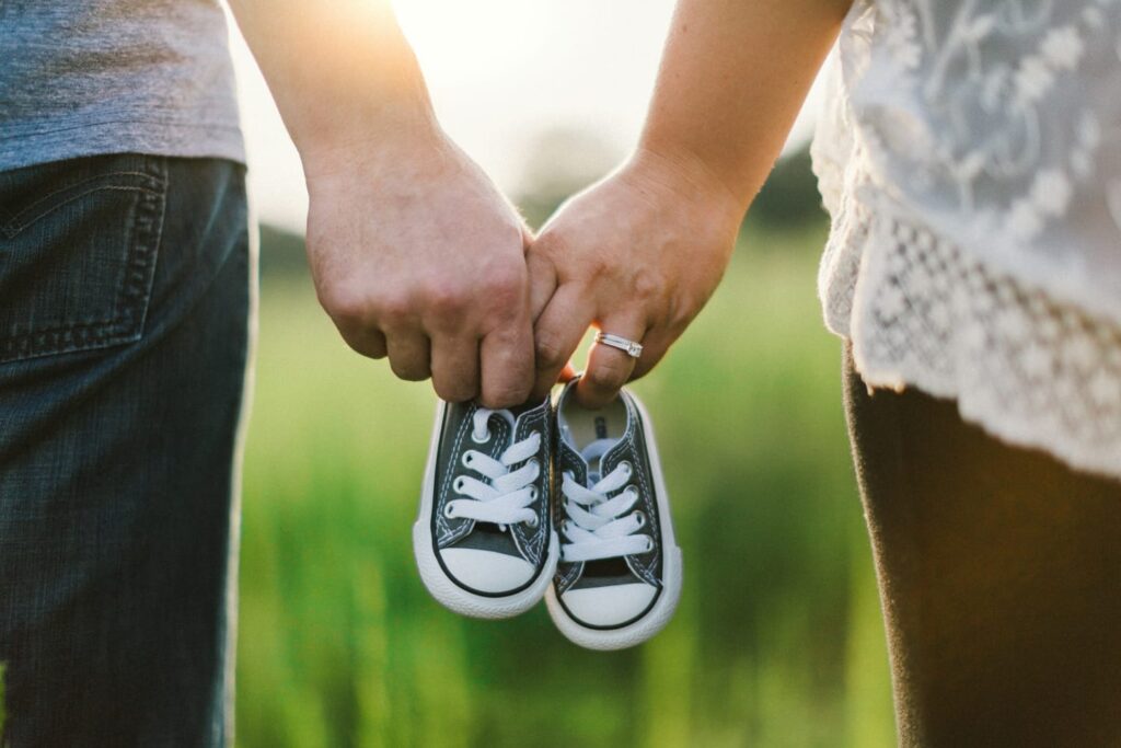 Casal de mãos dadas segurando sapatinhos de bebê, simbolizando o desejo de engravidar e cuidar da fertilidade.