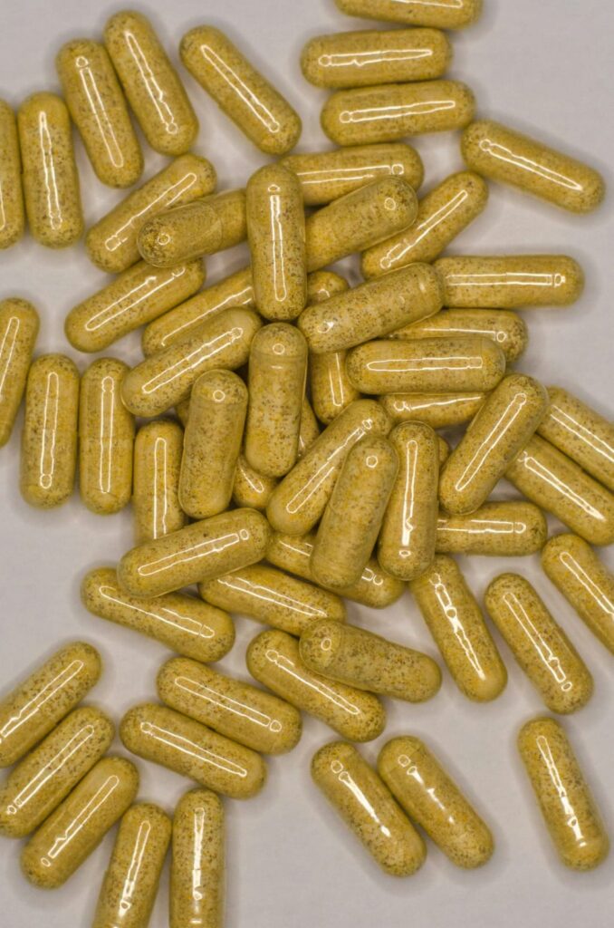 Cápsulas amarelas de suplemento de Vitamina K em superfície clara.