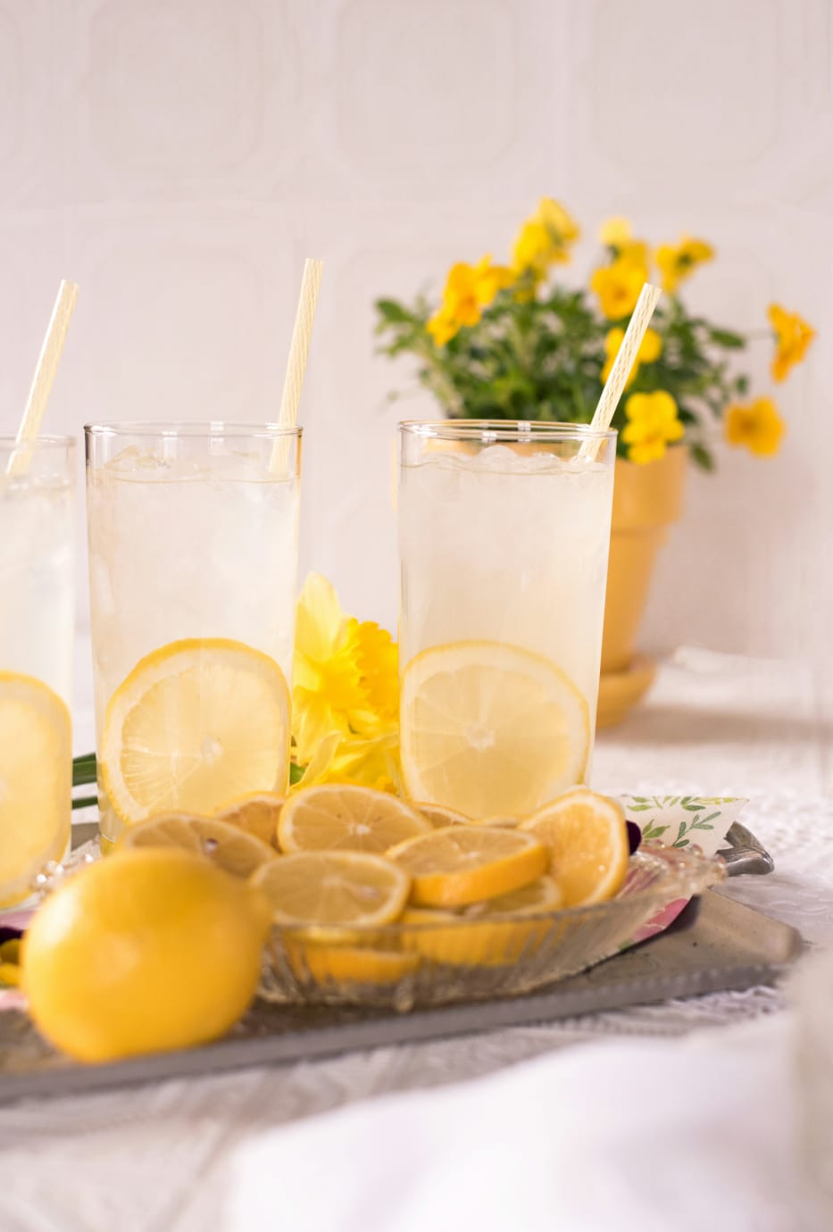 Copos de água com limão e rodelas frescas sobre uma mesa decorada, bebida leve e refrescante.