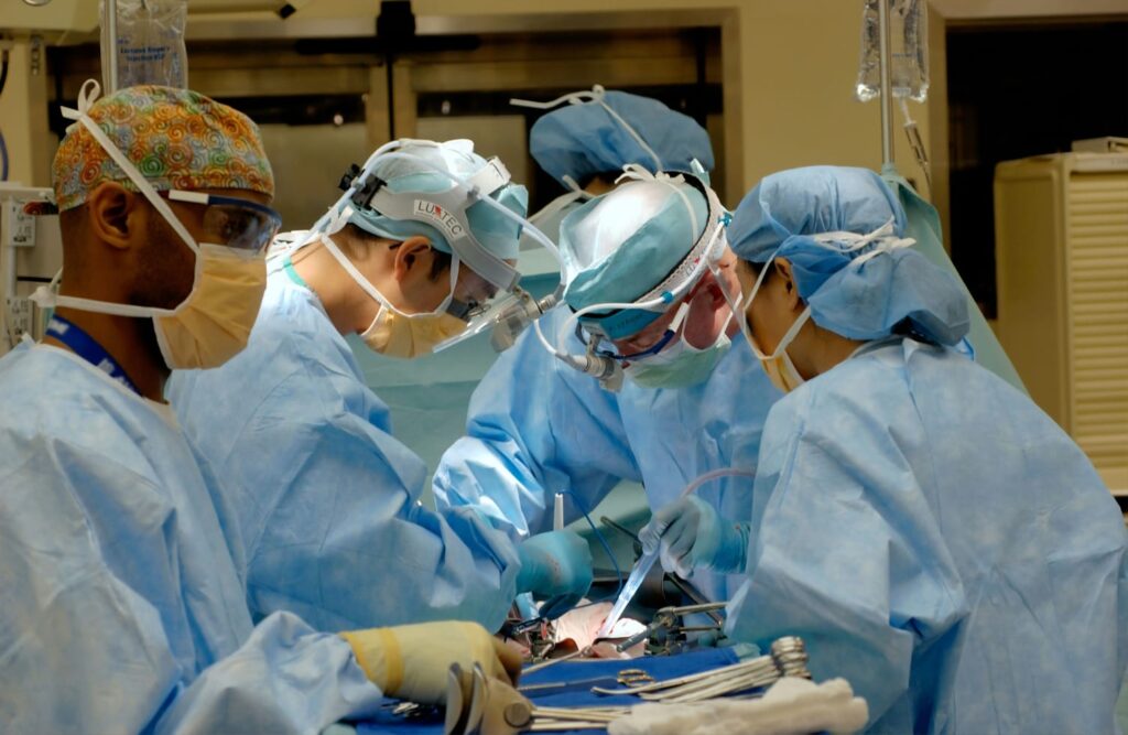 Equipe médica realizando uma cirurgia de transplante em uma sala cirúrgica, todos vestidos com roupas estéreis azuis.