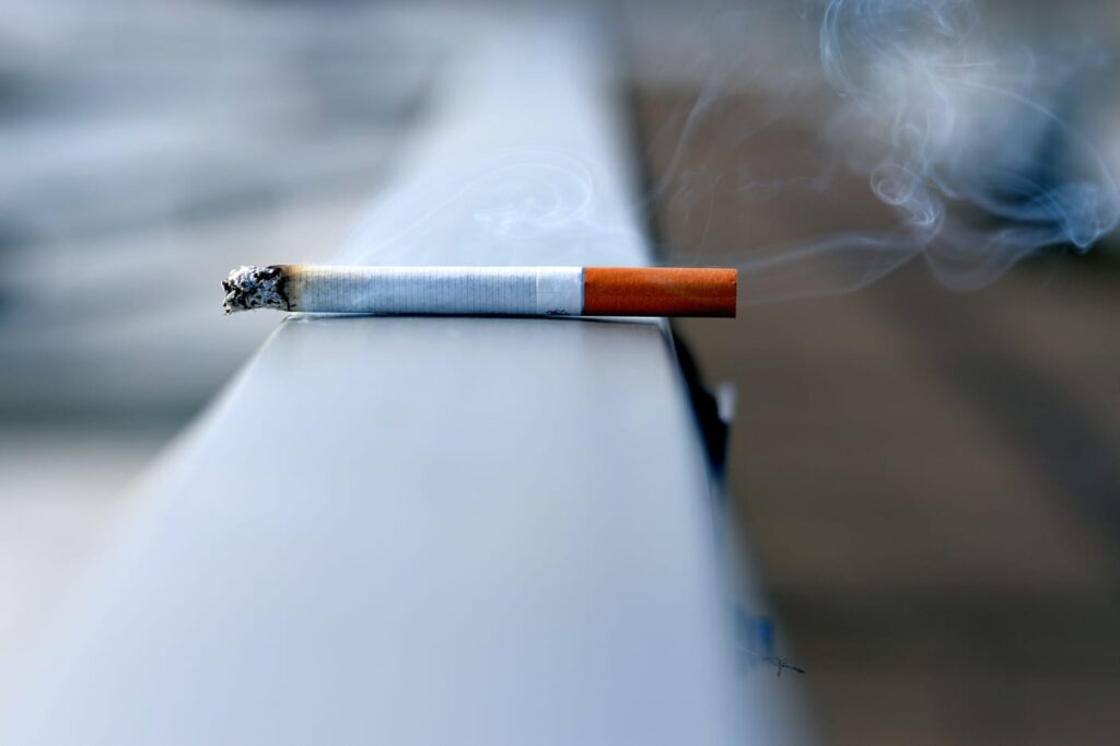 Cigarro aceso soltando fumaça, simbolizando os riscos do tabagismo.