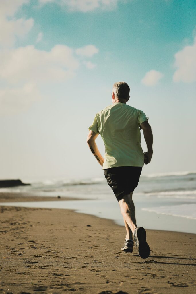 Homem correndo na praia, ilustrando como exercícios ajudam no controle das doenças crônicas.