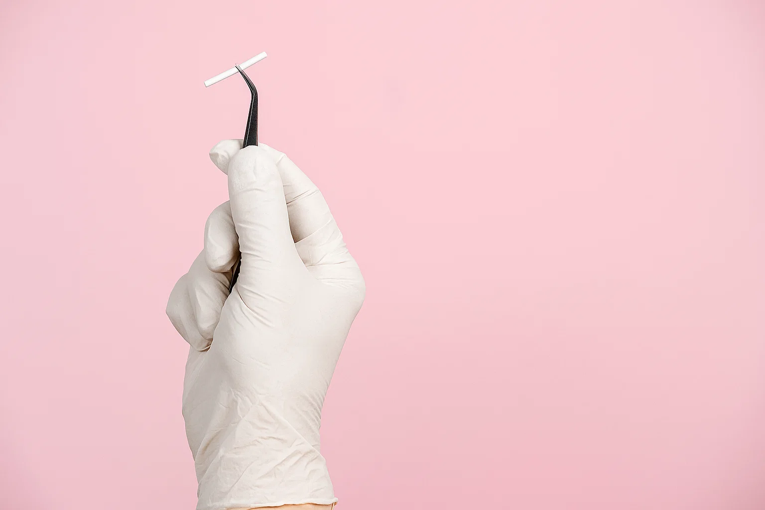 Profissional segurando o Implanon com pinça em frente a fundo rosa representando o implante e a dúvida frequente se Implanon engorda.