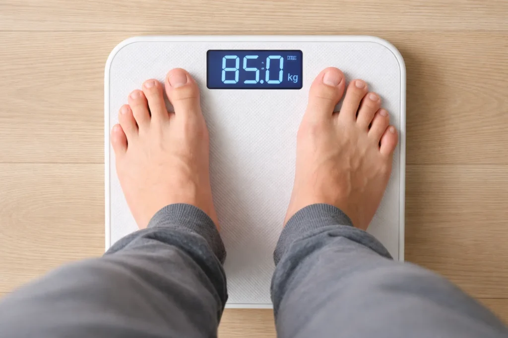 Pessoa em pé sobre uma balança digital marcando 85 kg, ilustrando a dúvida se exercício emagrece e a relação entre atividade física e perda de peso.